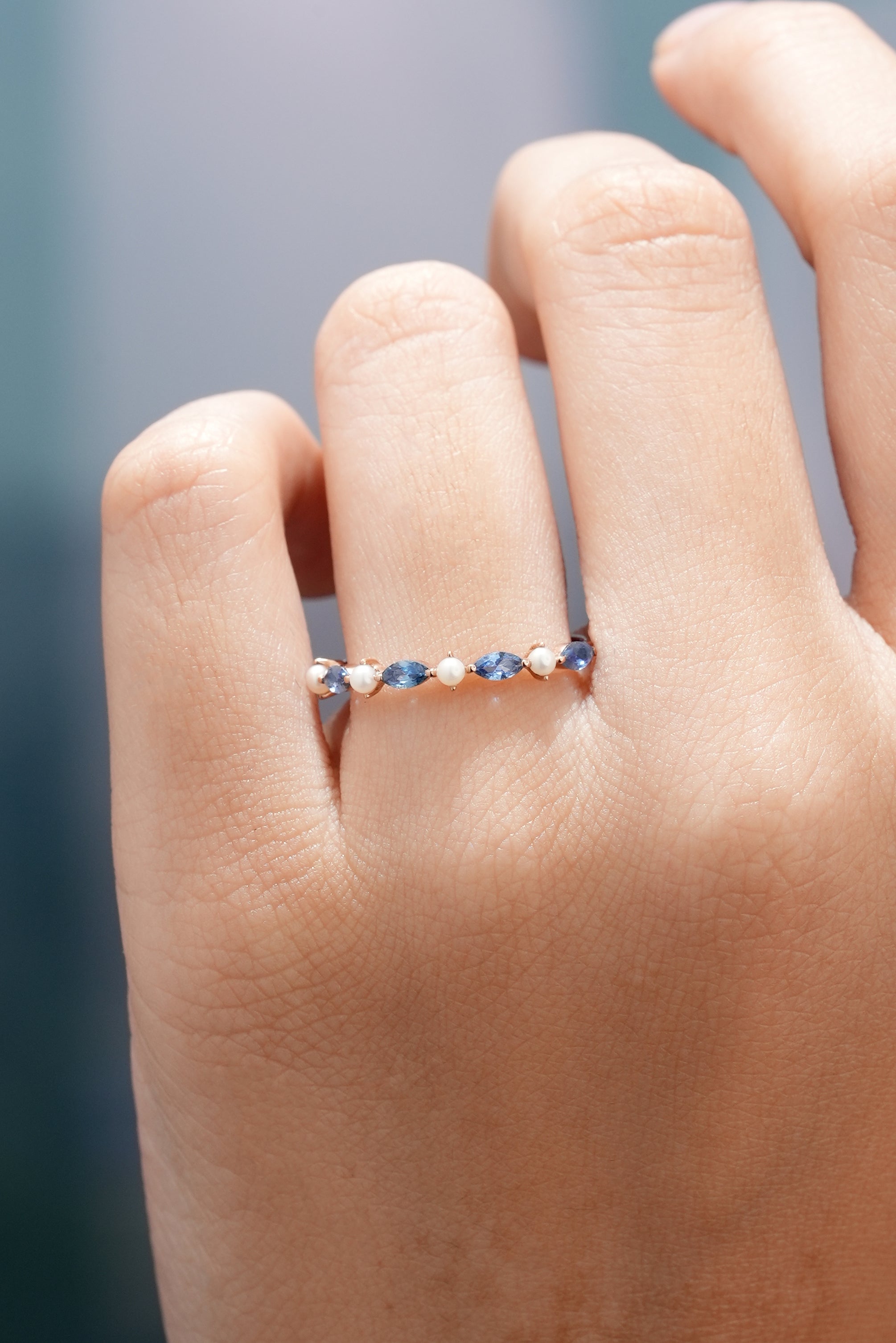 Marquise cut sapphire and pearl wedding band on a finger