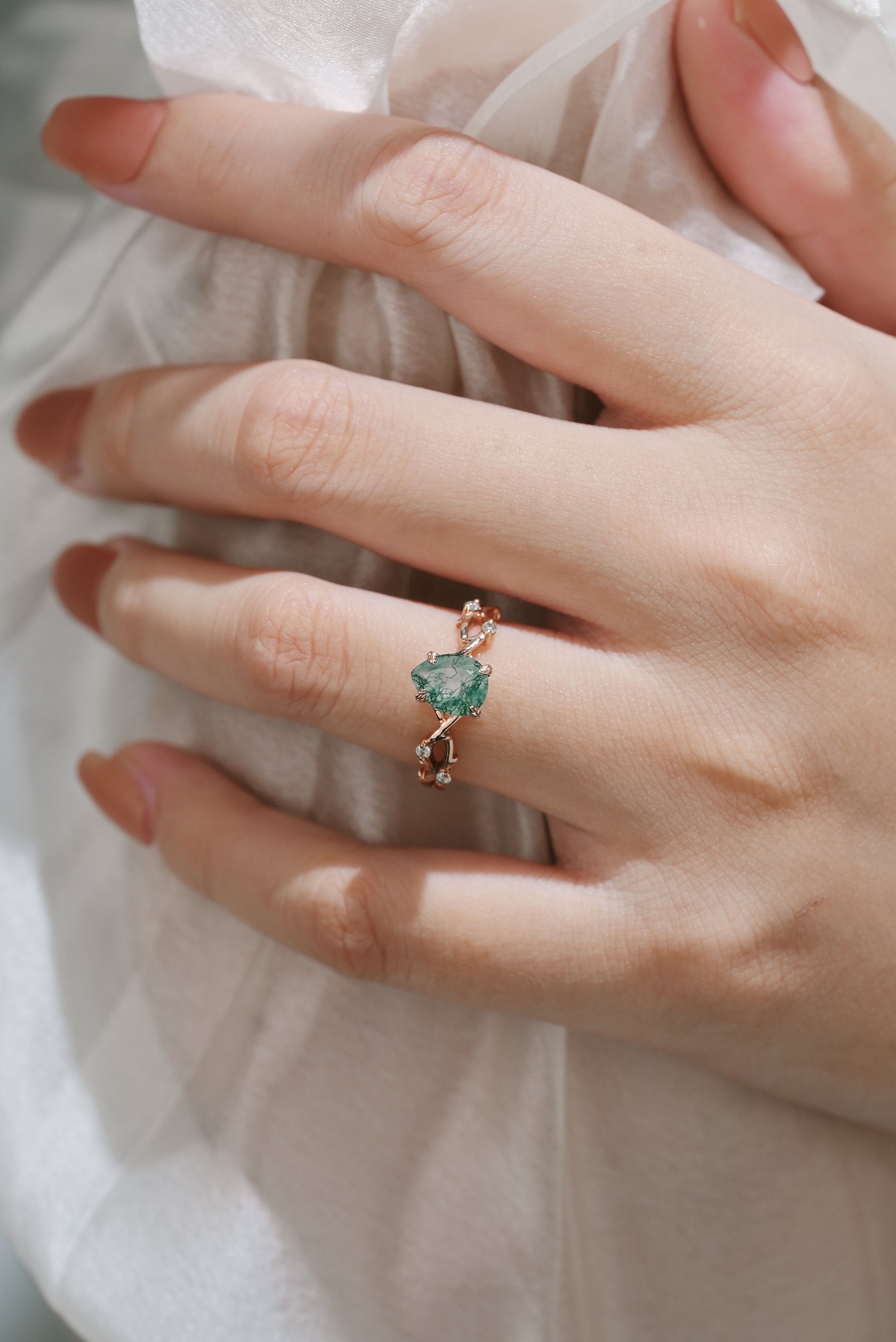 Hand holding a pear cut moss agate ring with vine leaf design