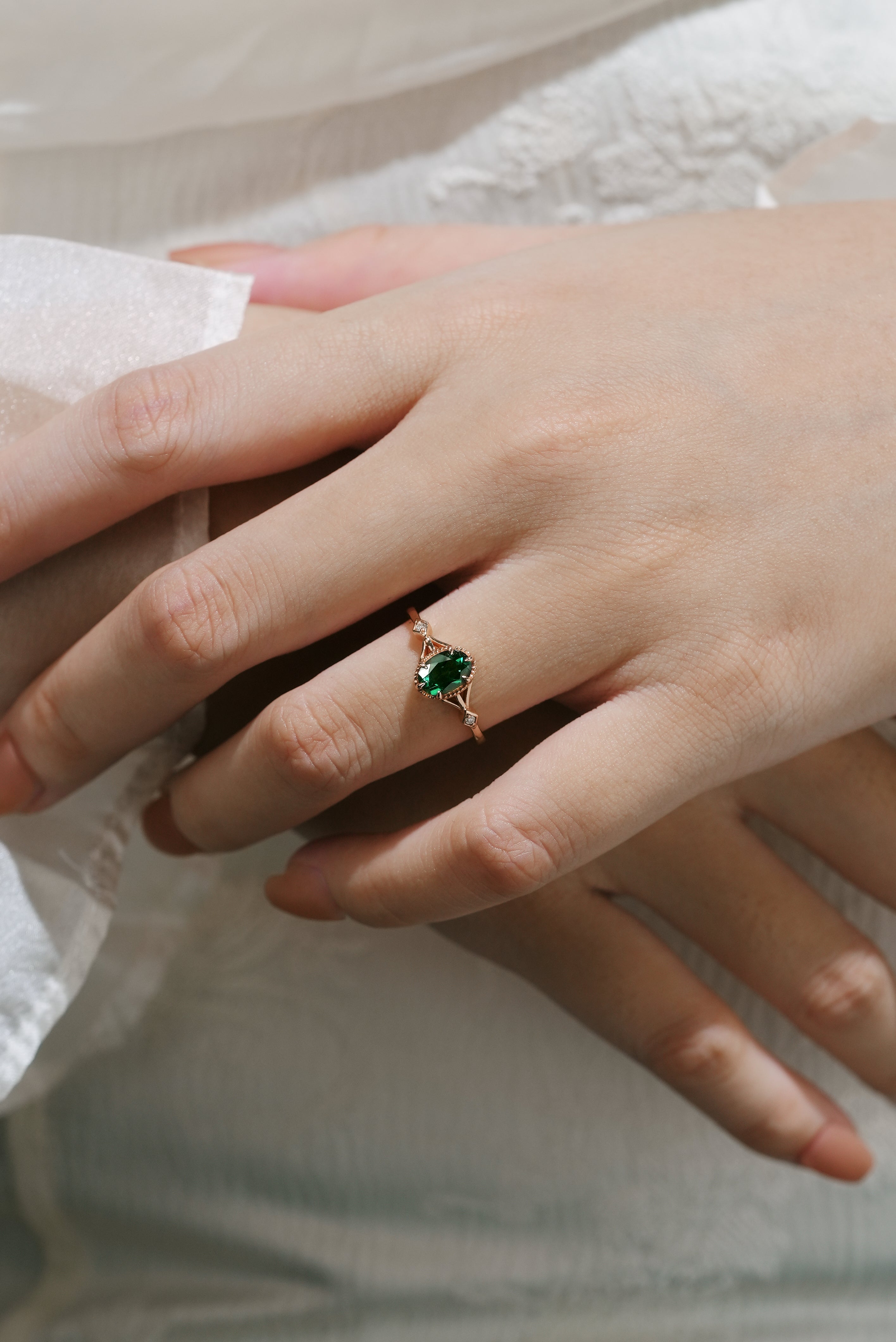 Oval emerald engagement ring on finger, nature-inspired rose gold design