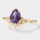 Pear-cut alexandrite engagement ring with leaf design, moissanite accents, and solid gold band.