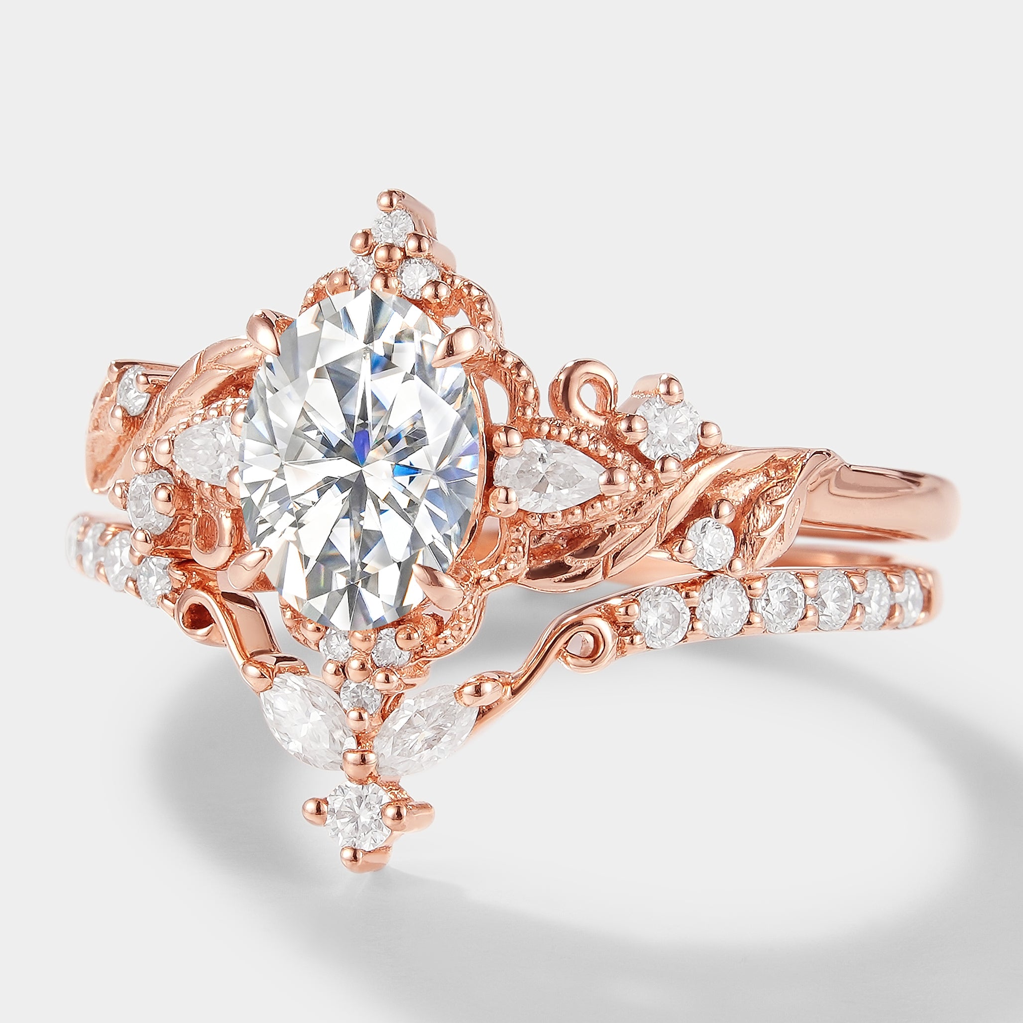 Rose gold leaf-inspired moissanite engagement ring set. Oval cut center stone, marquise and round accents, bridal ring set.