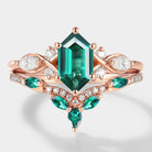 Rose gold ring set with a long hexagon-cut lab emerald and moissanite accents. Bridal ring set with emerald and moissanite.