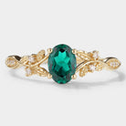 Oval lab-grown emerald engagement ring with leaf design and moissanite accents. Vintage-style