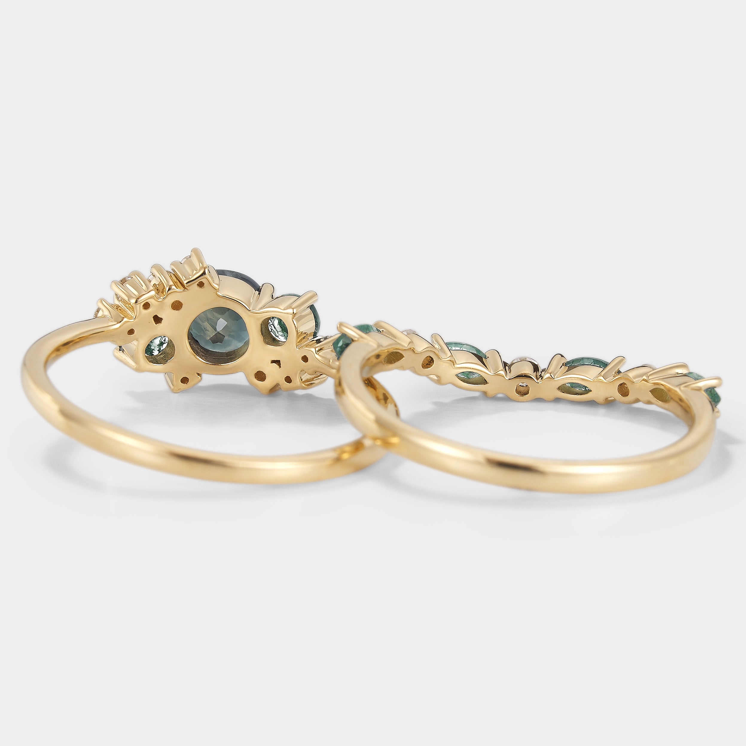 Close-up of a teal sapphire engagement ring and matching moissanite wedding band set in gold.